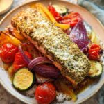 A perfectly cooked fillet of Pesto Salmon with Roasted Veggies served over rice on a light-colored plate.