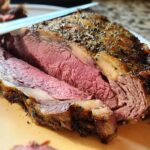 Close-up of a thick slice of medium-rare Prime Rib in a Roaster Oven, showing a seasoned crust and tender pink interior.