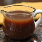 Close-up of a small glass gravy boat filled with rich and flavorful beef au jus recipe.
