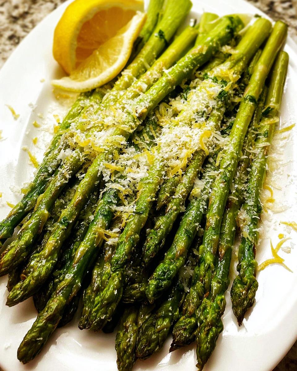 A plate of bright green Roasted Asparagus with Parmesan cheese and a lemon wedge garnish.