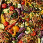 Overhead view of Sheet Pan Chicken & Veggies with roasted chicken thighs, peppers, onions, zucchini, tomatoes, and feta.