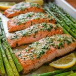 Four fillets of Garlic Butter Salmon & Asparagus baked on a sheet pan with lemon slices.