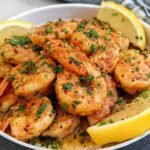 A close-up of cooked Garlic Butter Shrimp seasoned with paprika and parsley, served in a white bowl with lemon wedges.