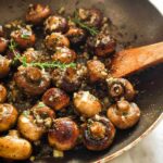 Close-up of whole button mushrooms simmering in a skillet with garlic butter sauce and fresh thyme, ready to serve.
