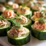 Close-up of several Smoked Salmon Cucumber Bites topped with dill and creamy salmon spread.