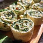 Close-up of several freshly cut Spinach Dip Pinwheels showing the creamy green spinach filling swirled inside a soft wrap.