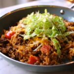 Close-up of a finished Taco Skillet meal in a light blue pan, topped with shredded lettuce and cheese.