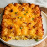 A square serving of Tater Tot Breakfast Casserole featuring a crispy tater tot crust and melted cheddar cheese topping.