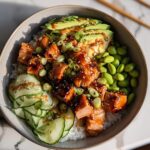 A vibrant bowl featuring glazed salmon chunks over rice, topped with avocado, edamame, and cucumber slices in a Teriyaki Salmon Bowls recipe.