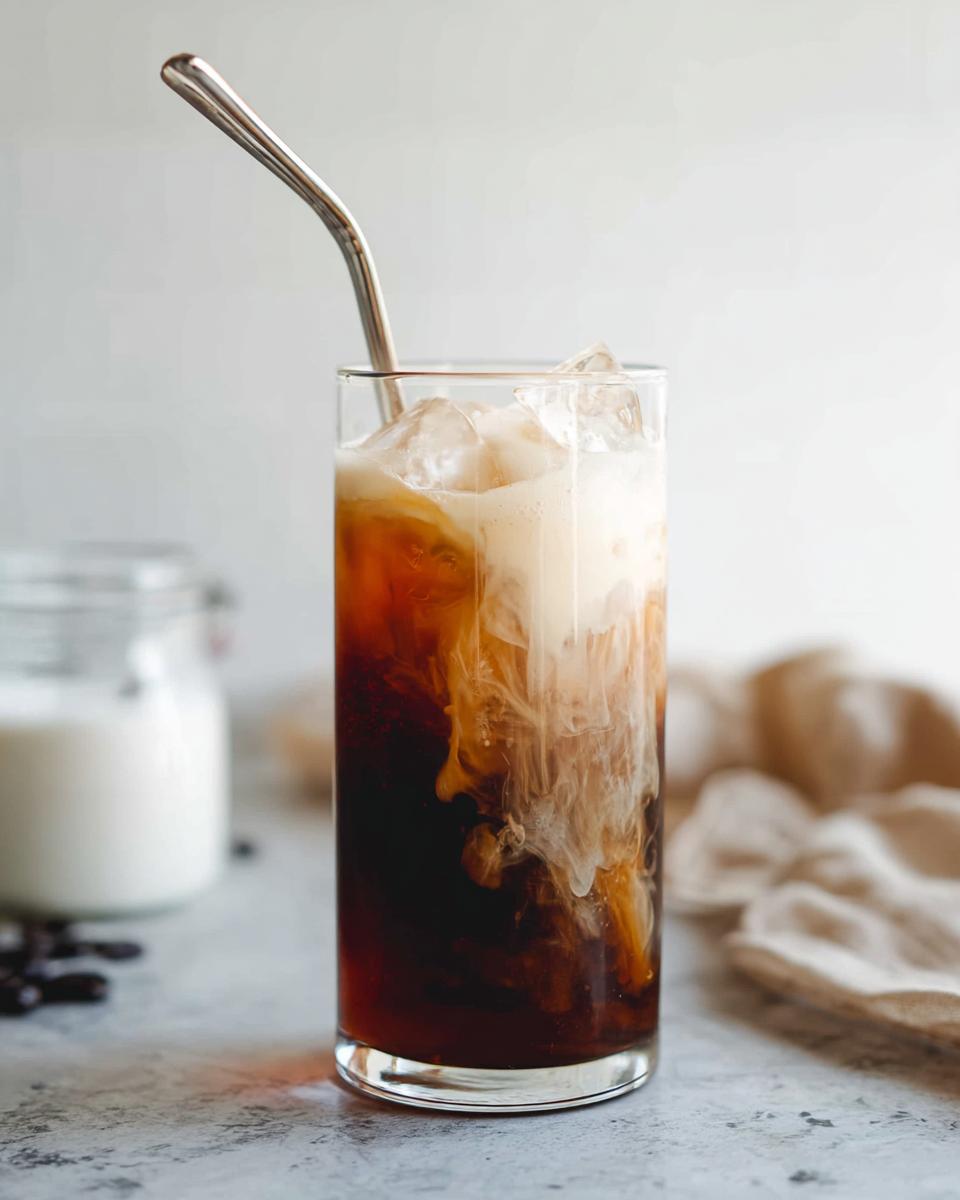 Close-up of Vanilla Sweet Cream Cold Foam Cold Brew with cream swirling into dark coffee over ice.