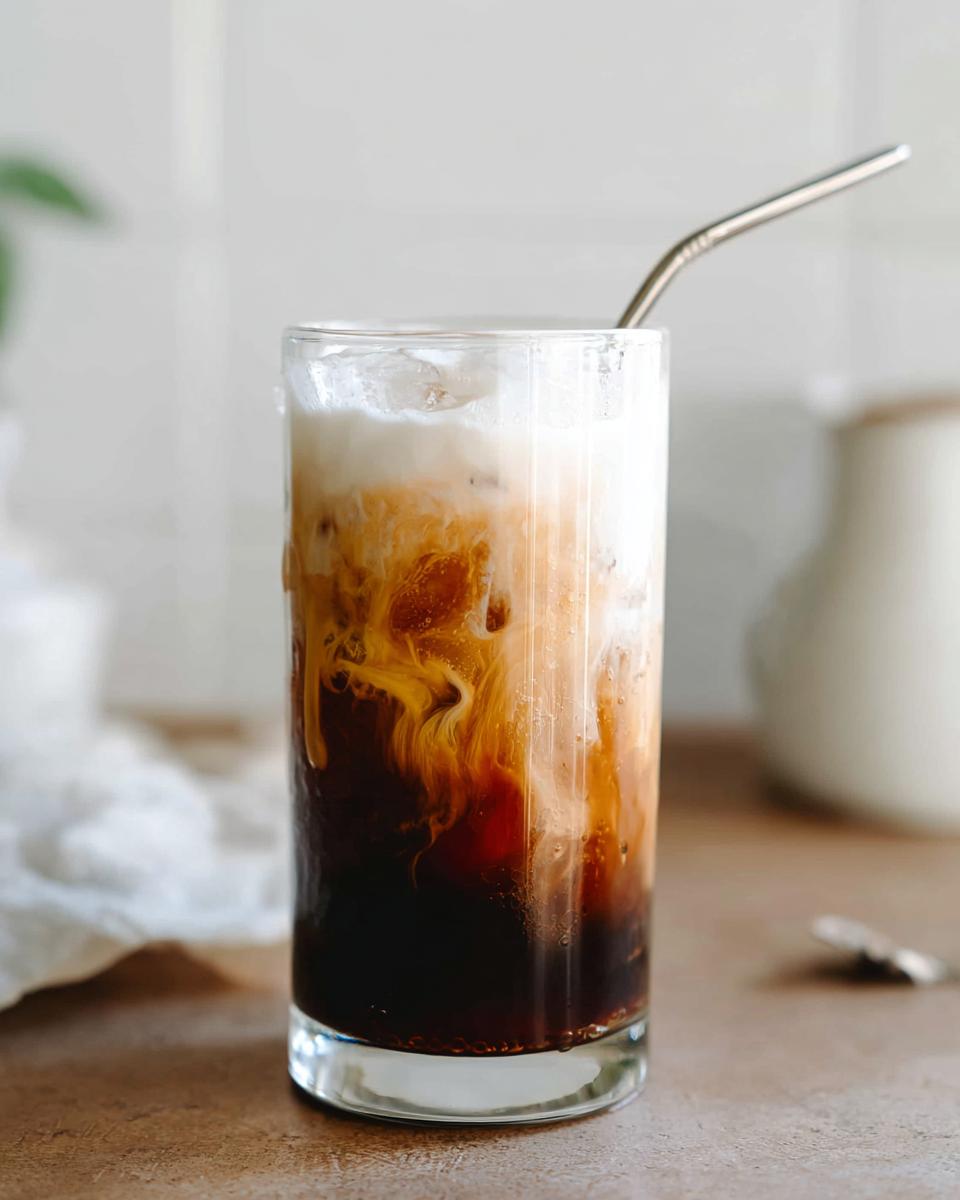 A tall glass filled with Vanilla Sweet Cream Cold Foam Cold Brew, showing the dark coffee swirling with the white foam.