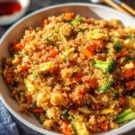 A close-up of a white bowl filled with vibrant Vegetable Quinoa Fried Rice, featuring quinoa, carrots, broccoli, and scrambled egg.