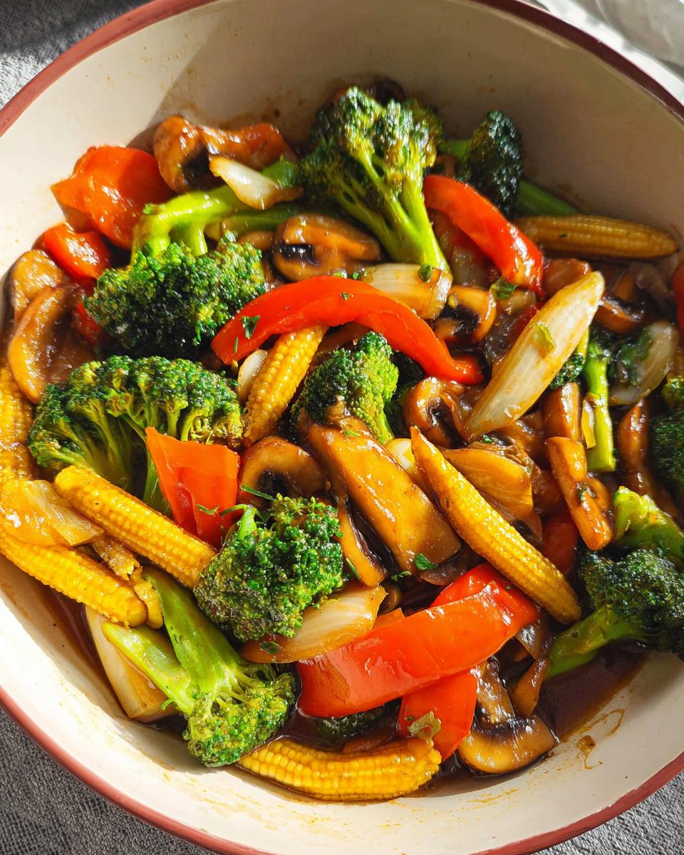 A vibrant bowl of Vegetable Stir Fry featuring broccoli, baby corn, red bell peppers, mushrooms, and onions in a glossy sauce.