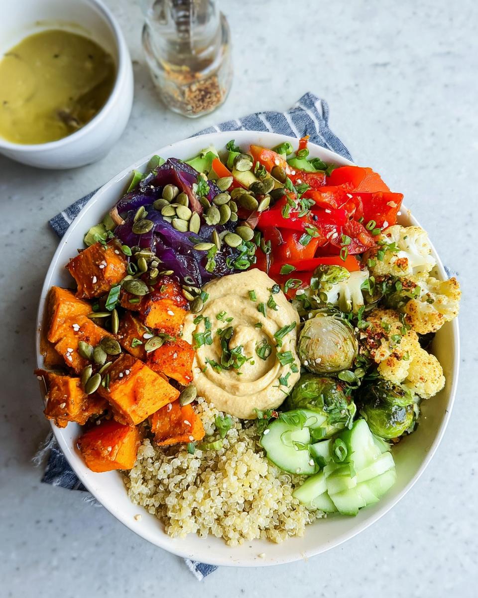 A vibrant bowl filled with quinoa, roasted sweet potatoes, Brussels sprouts, cauliflower, red peppers, purple cabbage, and hummus, perfect for Vegetarian Meal Prep Bowls.