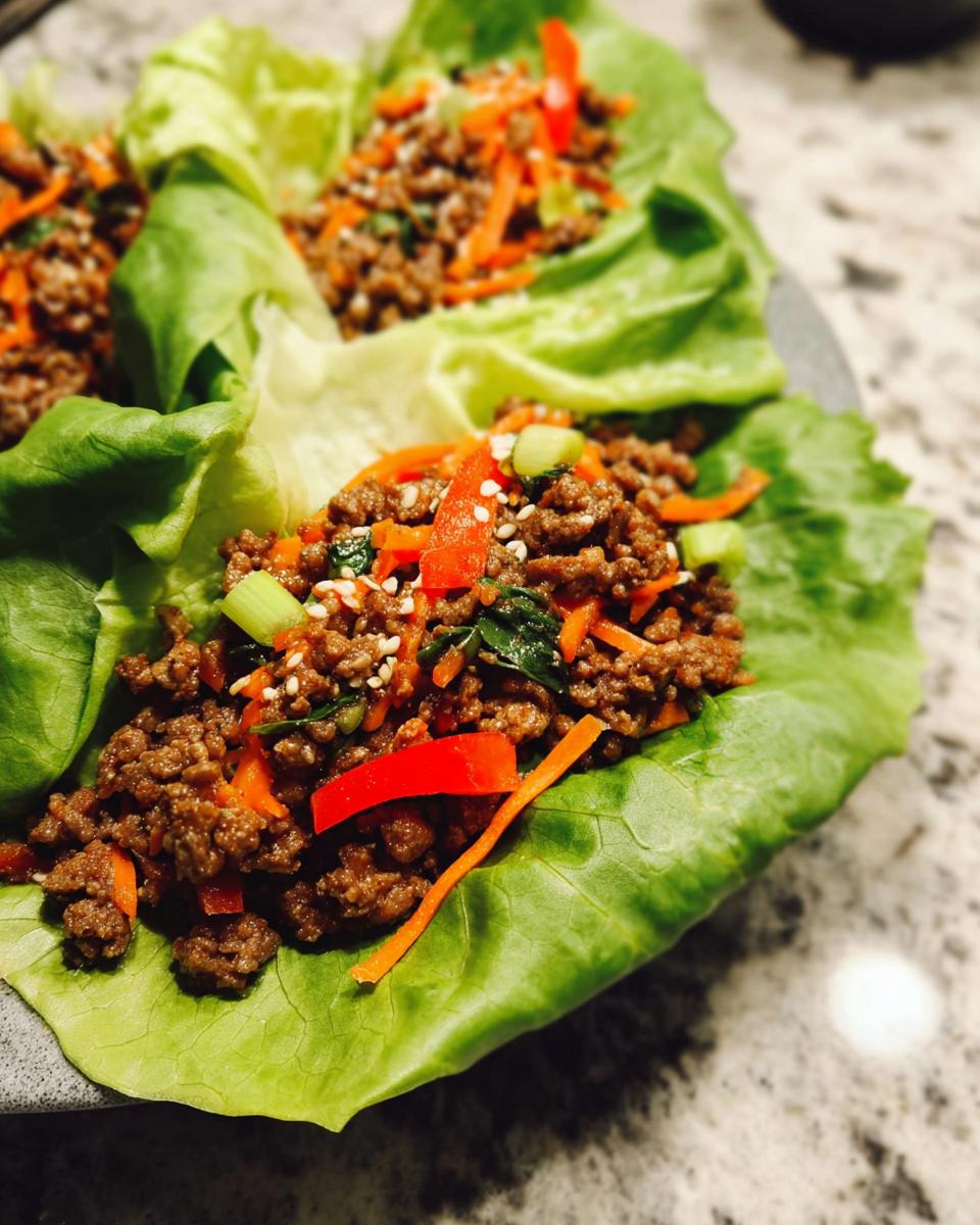 Close-up of Asian Ground Beef Lettuce Wraps filled with seasoned meat, carrots, peppers, and sesame seeds.