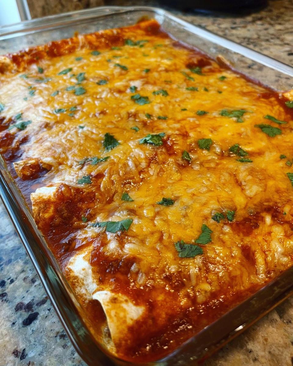 A close-up of freshly Baked Cheesy Beef Enchiladas covered in melted orange cheese and cilantro.