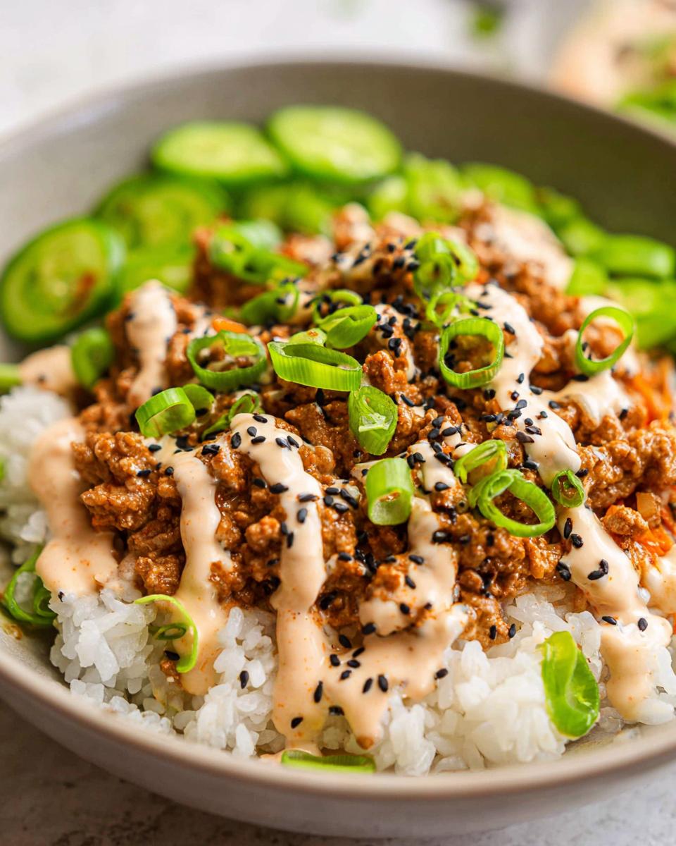 A close-up of Bang Bang Ground Turkey Rice Bowls featuring seasoned ground turkey over white rice, drizzled with sauce and topped with green onions and black sesame seeds.