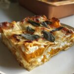 A perfect slice of Butternut Squash and Sage Lasagna, layered with orange squash, ricotta, and topped with browned cheese and sage leaves.