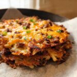 A crispy, golden-brown portion of Cheesy Potato Hash with Sausage Skillet, topped with melted cheddar and green onions.