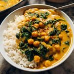A white bowl filled with white rice topped with vibrant Chickpea and Spinach Coconut Curry, garnished with chili flakes.