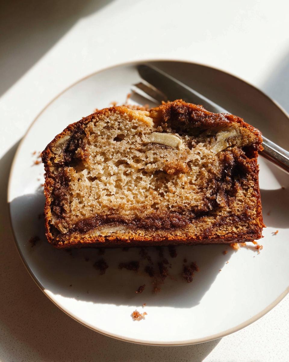 Close-up of a moist slice of Cinnamon Swirl Banana Bread on a white plate with crumbs.