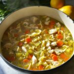Close-up of steaming Classic Homestyle Chicken Noodle Soup filled with broth, egg noodles, carrots, celery, and chicken pieces.