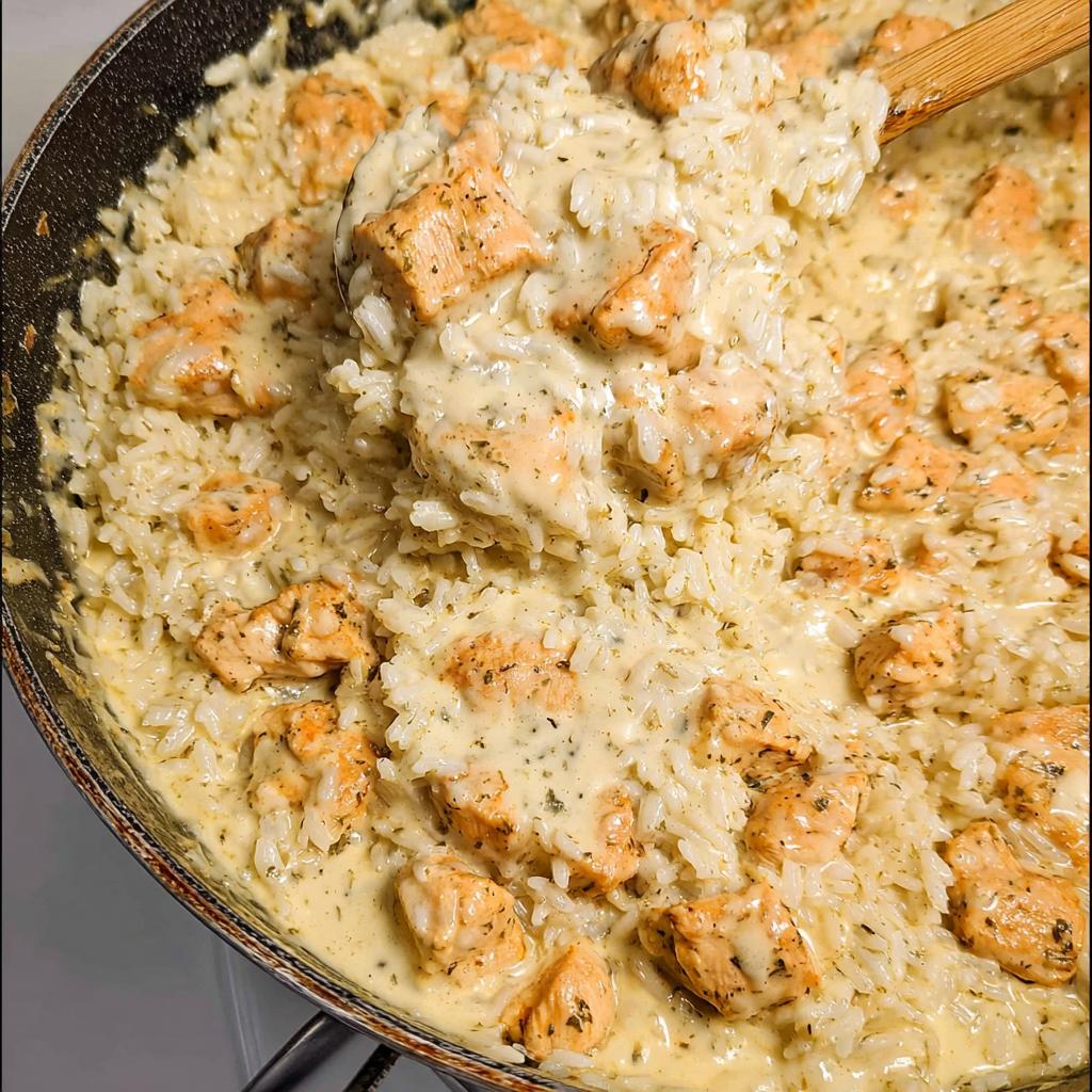 A close-up view of the finished Creamy Chicken and Rice Skillet being stirred with a wooden spoon in a black pan.