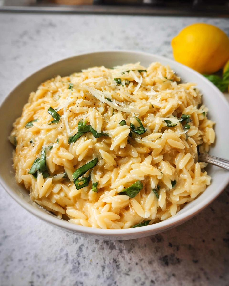 A close-up of creamy Lemon Parmesan Orzo topped with shredded cheese and fresh basil in a white bowl.