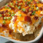A spoonful of creamy Loaded Baked Potato Casserole topped with melted cheddar, bacon bits, and green onions.