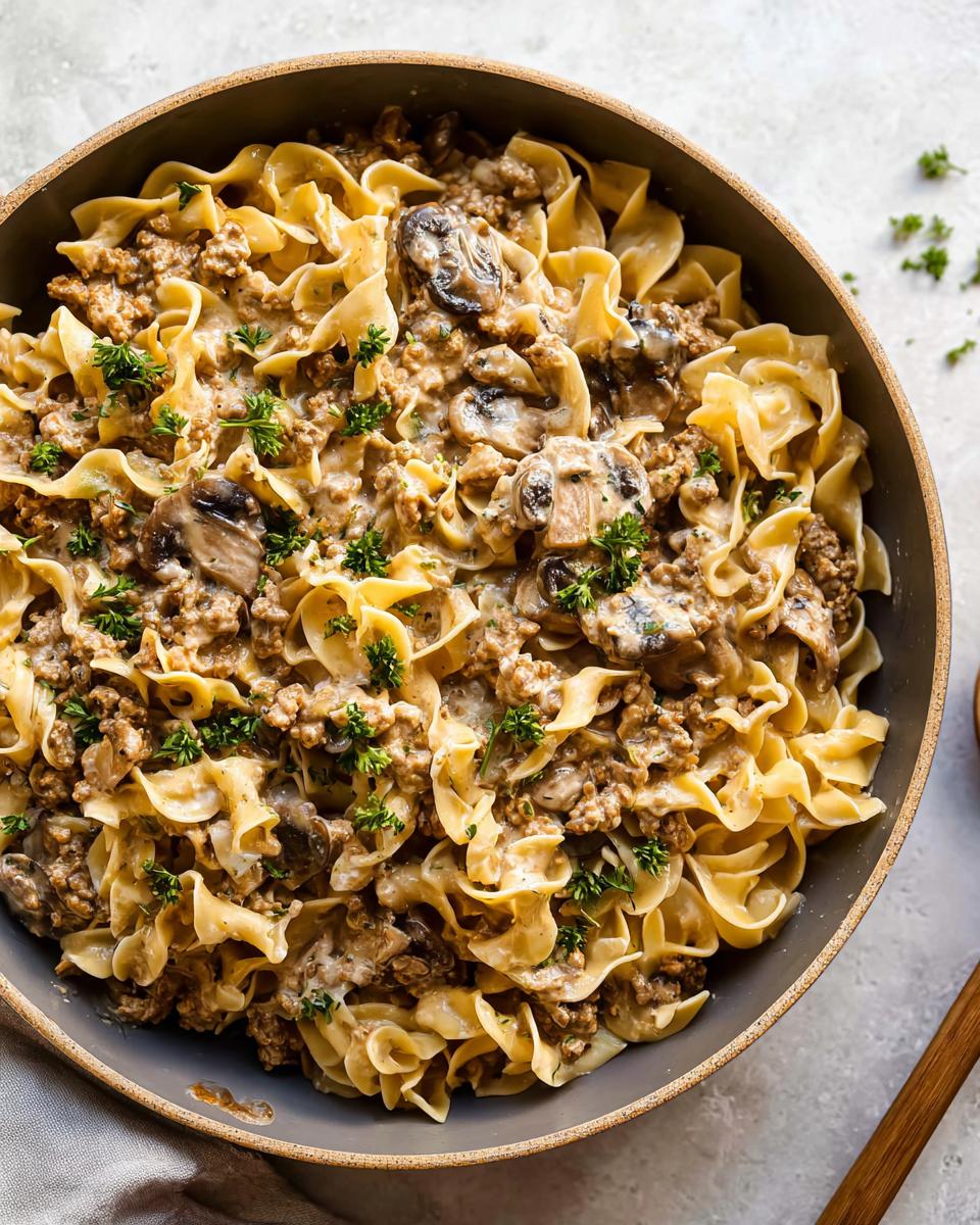 Overhead view of a bowl filled with Creamy Turkey Stroganoff mixed with egg noodles and sliced mushrooms, garnished with parsley.
