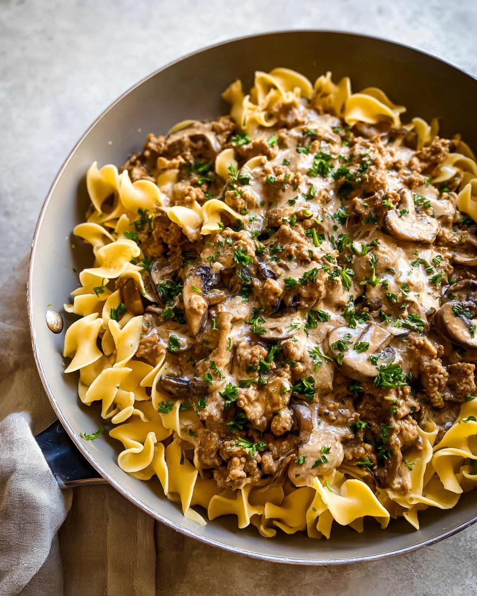 Close-up of Creamy Turkey Stroganoff served over egg noodles in a skillet, topped with mushrooms and parsley.