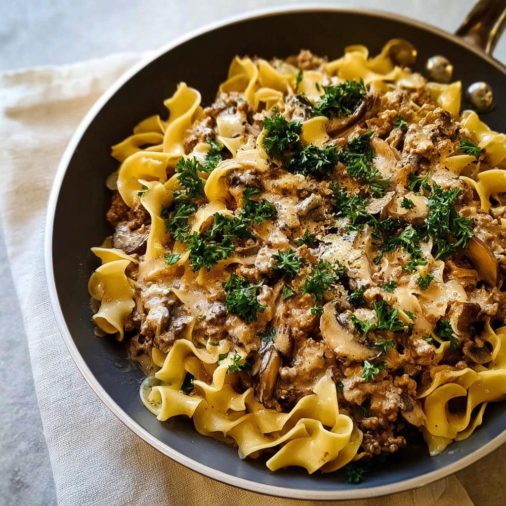 Close-up of Creamy Turkey Stroganoff served over egg noodles in a skillet, garnished with fresh parsley.