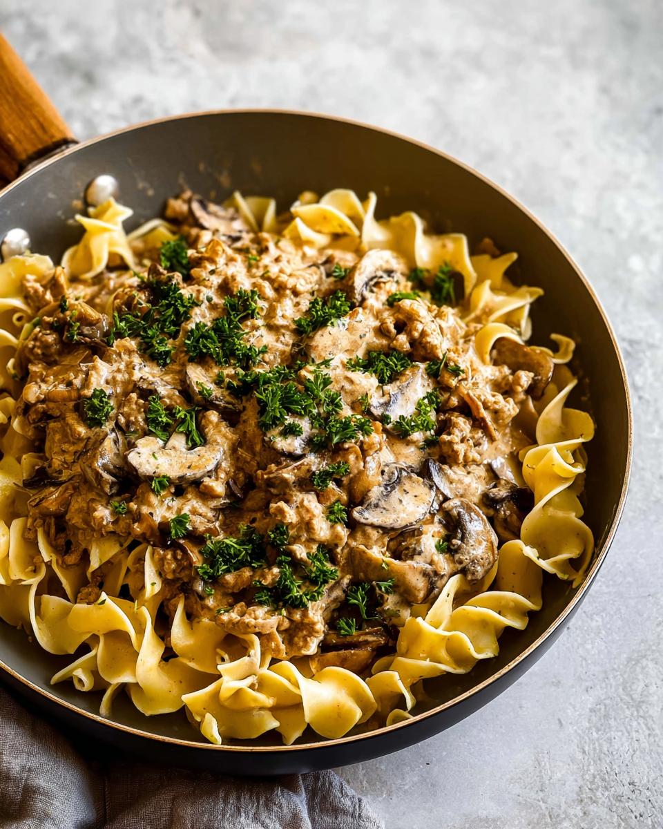 Close-up of Creamy Turkey Stroganoff served over egg noodles in a dark skillet, topped with fresh parsley.