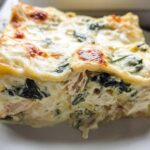 A close-up of a thick, cheesy slice of Creamy White Chicken Spinach Lasagna on a white plate.