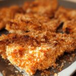 Close-up of golden brown, crispy breaded pieces of Buttermilk Baked Fried Chicken on a gray tray.