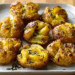 Close-up of golden brown, crispy smashed potatoes drizzled with herbed butter.