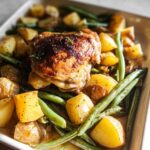 Crispy Garlic Butter Baked Chicken Thighs and Potatoes with green beans in a white baking dish.
