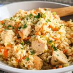 Close-up of a bowl filled with Healthy One Pot Chicken and Brown Rice, mixed with carrots and garnished with parsley.