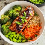 A close-up of a Healthy Teriyaki Salmon and Broccoli Bowls featuring glazed salmon, brown rice, edamame, and shredded carrots.