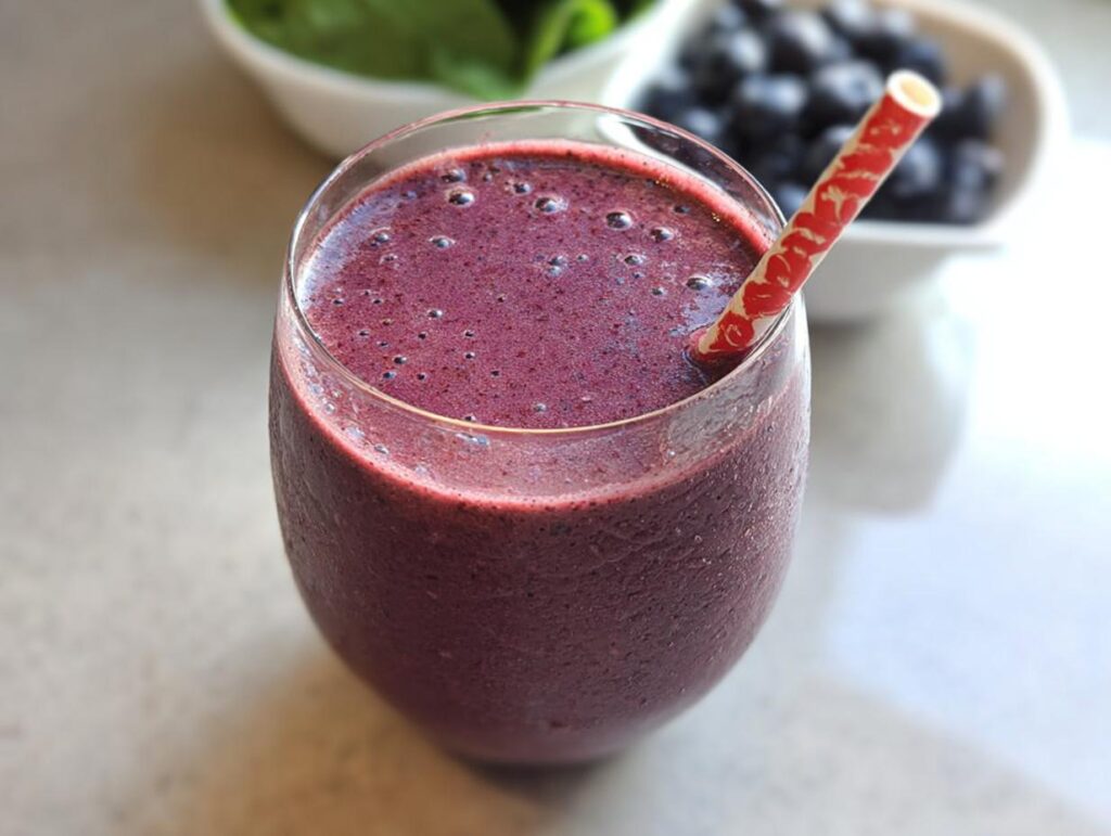 Close-up of a thick, purple high-protein smoothie with a patterned straw, with blueberries visible in the background.