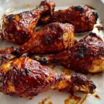 Five glistening Honey BBQ Baked Chicken Legs coated in a thick, dark sauce resting in a white baking dish.
