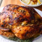 A beautifully browned Lemon Herb Whole Roasted Chicken resting on a white platter, garnished with fresh thyme.