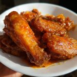 Close-up of several glossy, orange-glazed Mango Habanero Hot Wings piled on a white dish.
