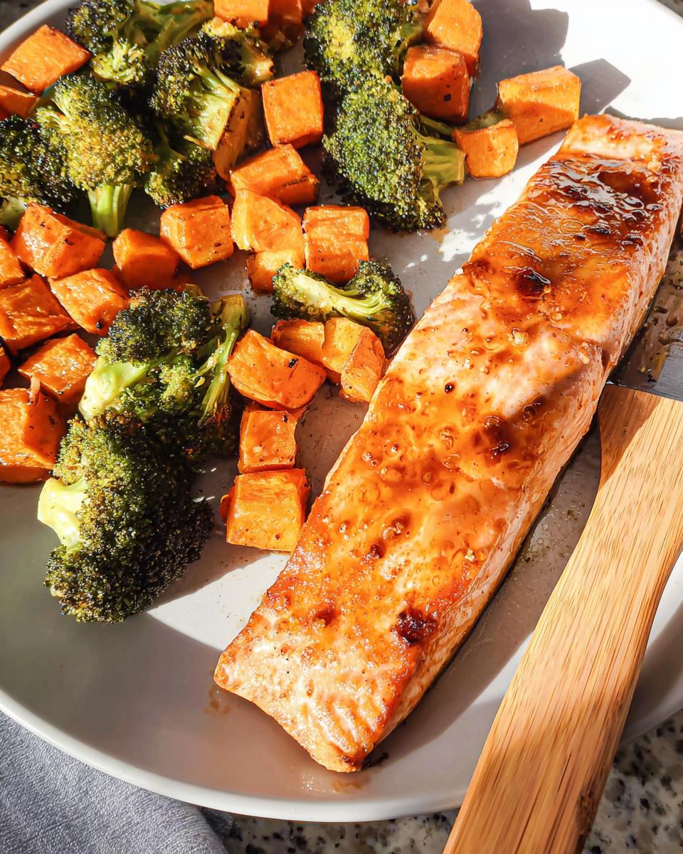 A cooked fillet of Maple Dijon Salmon Sheet Pan Dinner served with roasted sweet potatoes and broccoli florets.