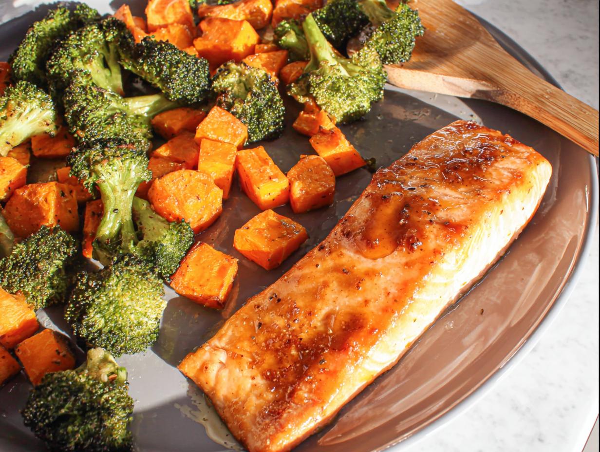 A cooked fillet of salmon glazed with maple dijon sauce served alongside roasted broccoli and sweet potatoes in a Maple Dijon Salmon Sheet Pan Dinner.