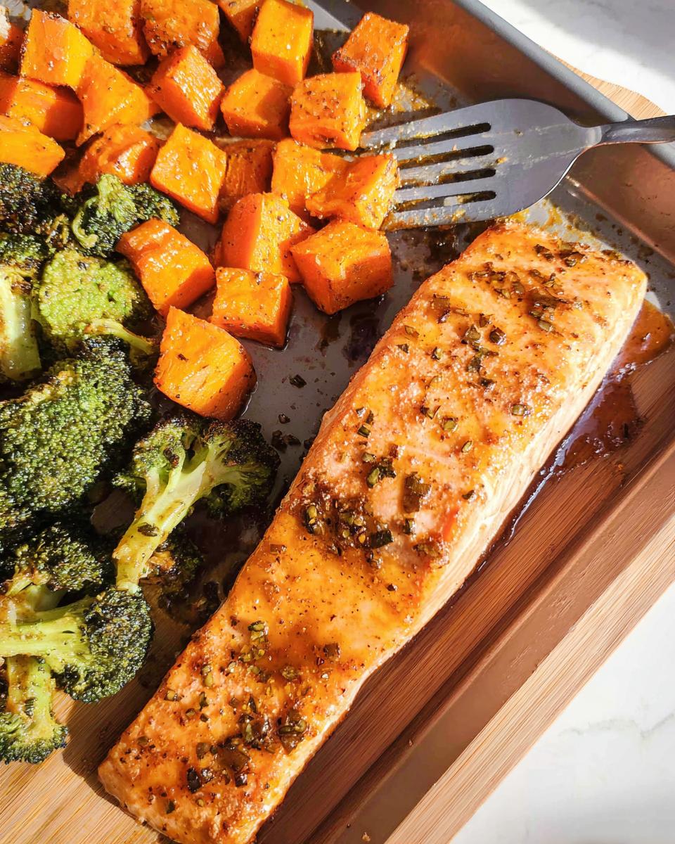A perfectly cooked fillet of Maple Dijon Salmon Sheet Pan Dinner served alongside roasted broccoli and sweet potatoes on a baking tray.