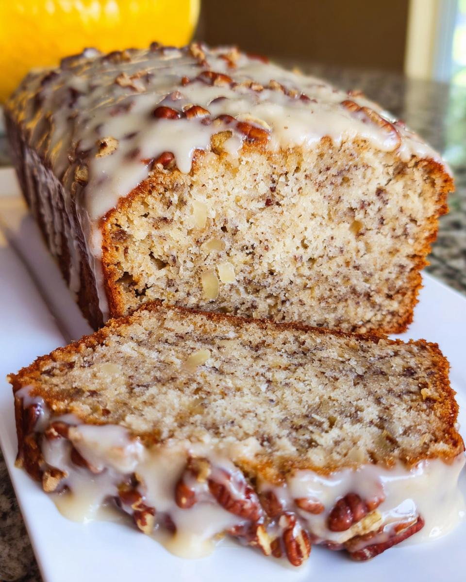 A loaf of Maple Pecan Banana Bread, sliced, showing the moist interior and topped with a thick maple glaze and pecans.