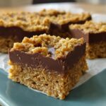A close-up of a layered No Bake Chocolate Peanut Butter Oat Bar showing the oat base, chocolate layer, and crumbly topping.