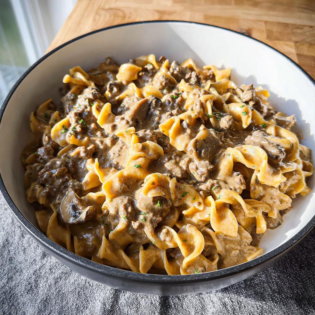 A close-up of creamy One Pot Ground Beef Stroganoff mixed with egg noodles and mushrooms in a white bowl.
