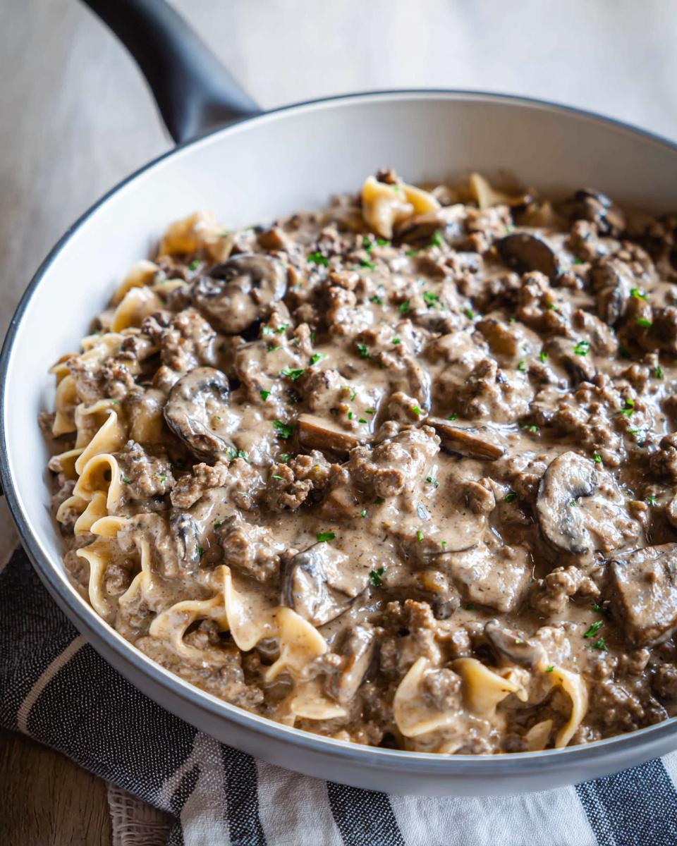 Close-up of creamy One Pot Ground Beef Stroganoff with egg noodles and mushrooms in a white skillet.